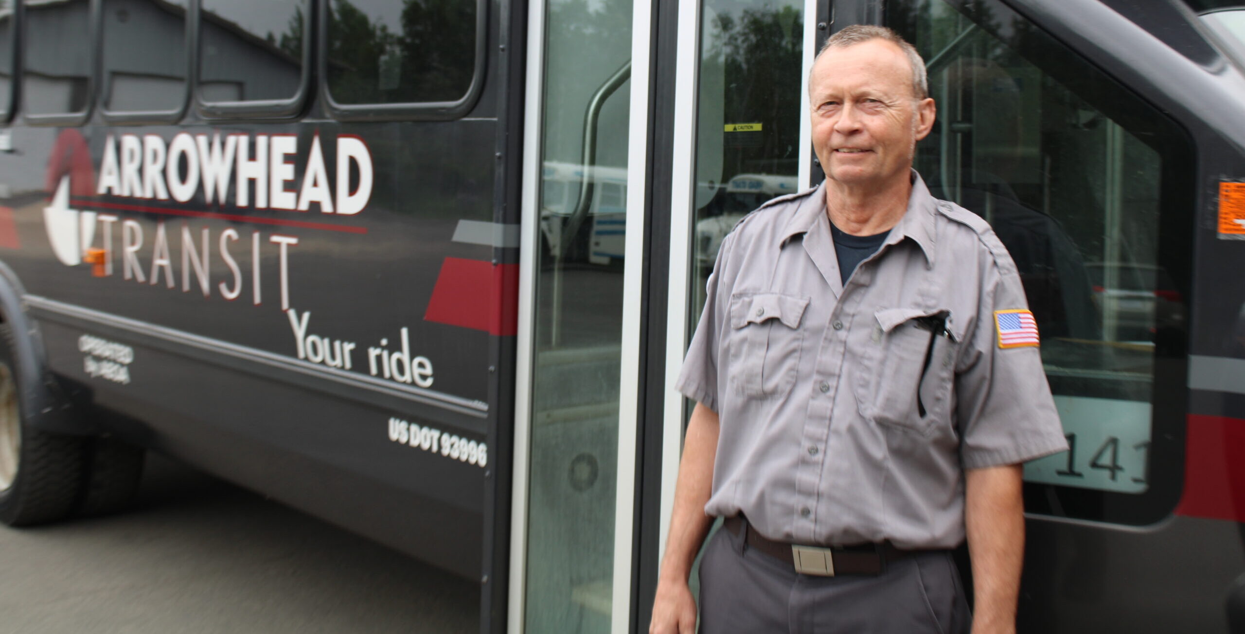 A bus driver stands outside of our handicap, ADA compliant bus and welcomes you on board with a smile.