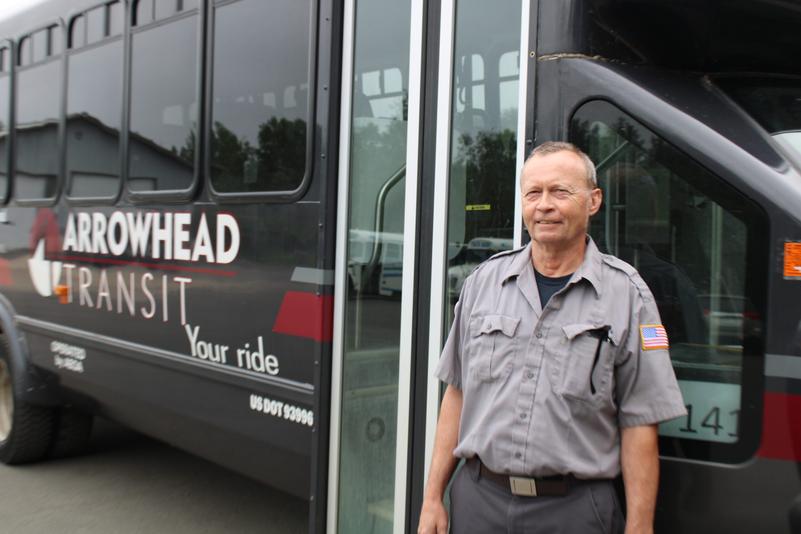 A bus driver stands outside of our handicap, ADA compliant bus and welcomes you on board with a smile.